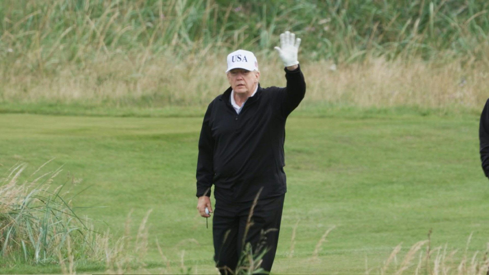 US President Donald Trump waves to media during a game of golf at his Turnberry resort